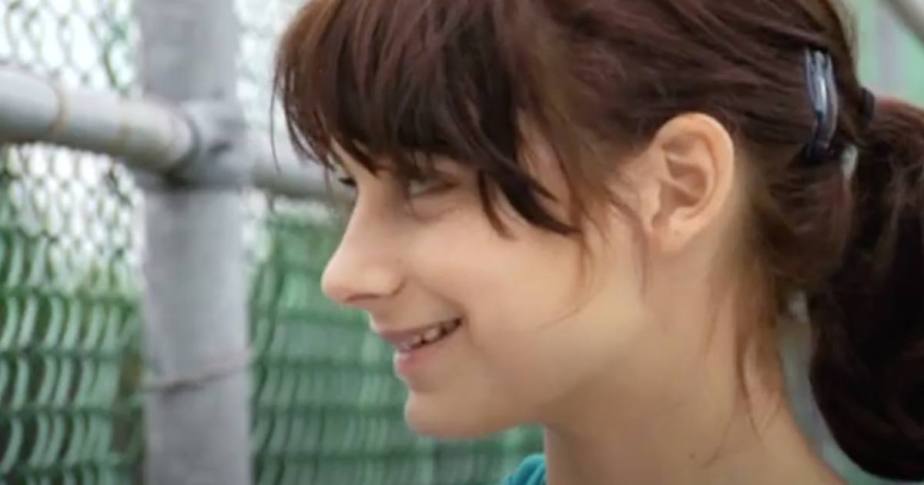 Une jeune fille à la queue de cheval affiche un sourire éclatant, reflétant une attitude joyeuse et accueillante. Sophie Desmarais